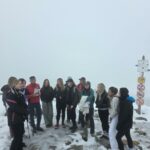 Grupa studentów ustawiona w półkolu, po prawej drogowskaz ze szlakami, tło to mgła